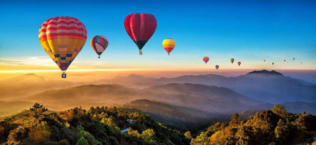 Grote groep luchtballonnen boven een mistig berglandschap
